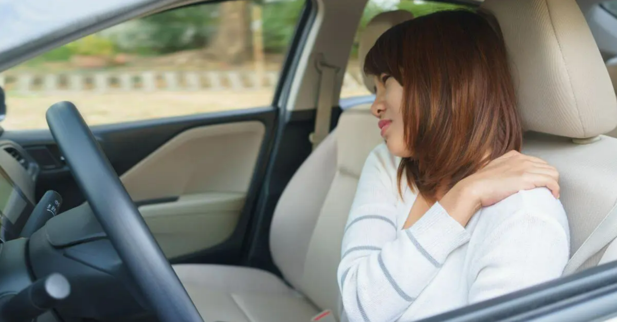 Woman sitting in car while holding left shoulder in pain