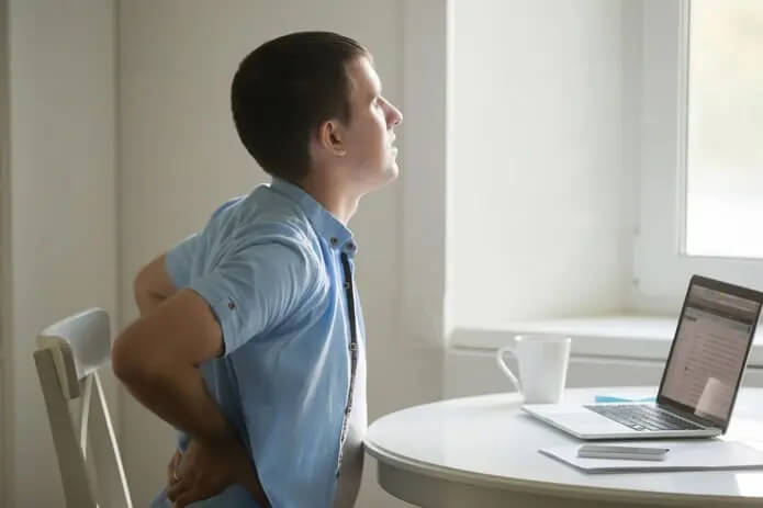 Young man holding lower back while sitting at table