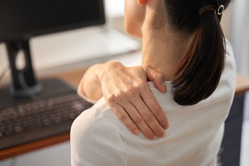 Mujer frente al ordenador sujetándose el hombro con dolor