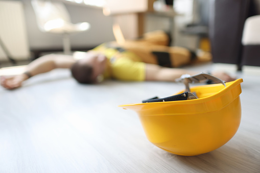 Yellow safety helmet on ground with injured worker in background