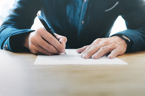 Homem de terno com caneta assinando um documento