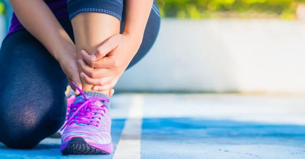 Mujer sujetándose el tobillo con dolor mientras lleva zapatillas de correr