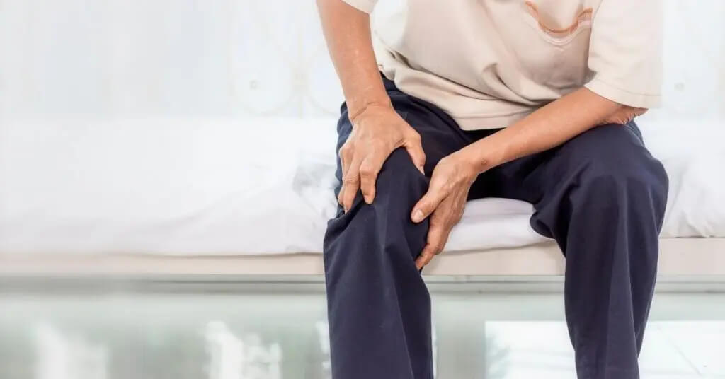 Sitting man holding knee in pain