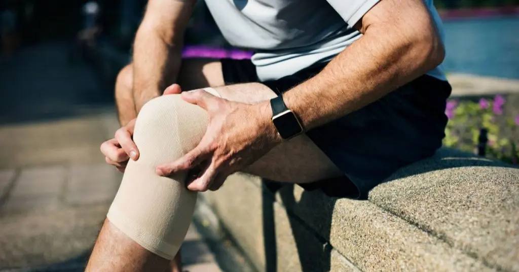 Man holding knee while wearing compression sleeve