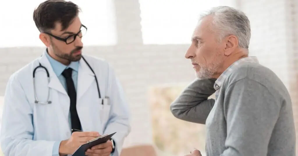 Médico de la columna vertebral en consulta con un paciente varón de edad avanzada